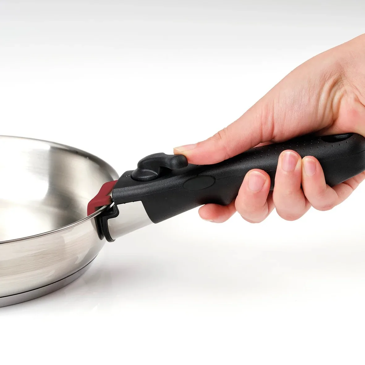 Main tenant une poêle inox avec la poignée amovible noire et rouge